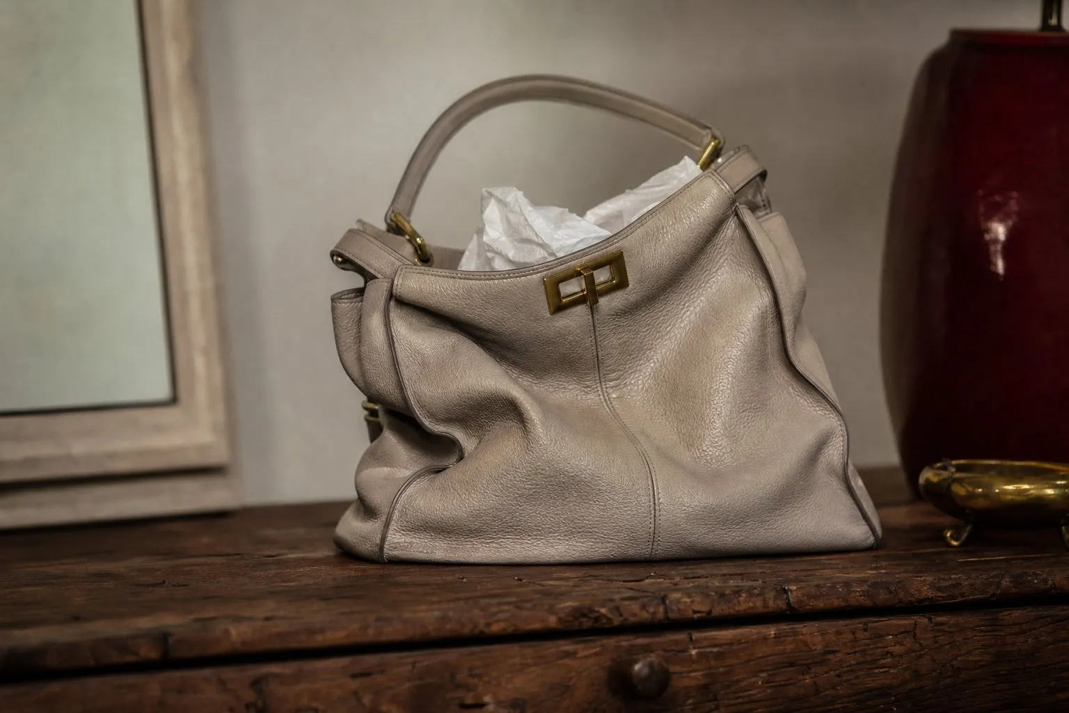 Sac a main en cuir souple pose sur une table en bois, flanc affaisse visible, a cote dun coussin de bourrage en tissu